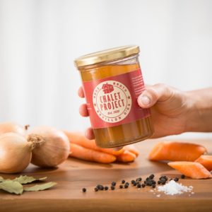 Main tenant un bocal de bouillon d'os de bœuf bio Chalet Project | Carottes, oignons, laurier, épices | Alimentation postpartum
